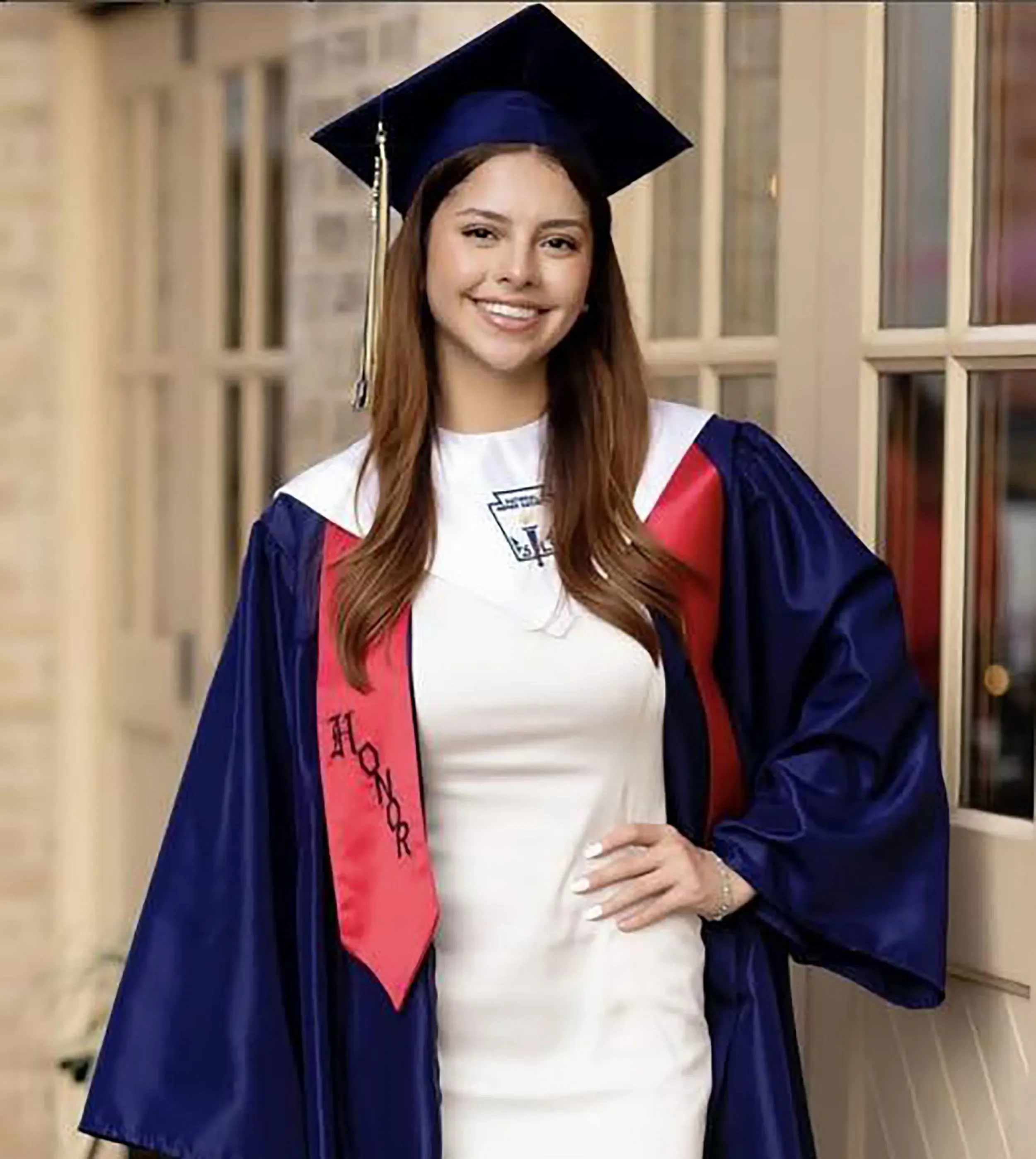 صورة لشابة ترتدي قبعة تخرج وزي تخرج رسمي، مبتسمة أمام مبنى، تمثل كاميلا ميندوزا أولموس المفقودة في سان أنطونيو.