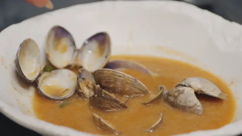 حساء الثوم الإسباني سوبا دي آجو في وعاء، يظهر فيه قشور المحار مع مرق غني، يعكس تقاليد الطهي في تشينتشون.