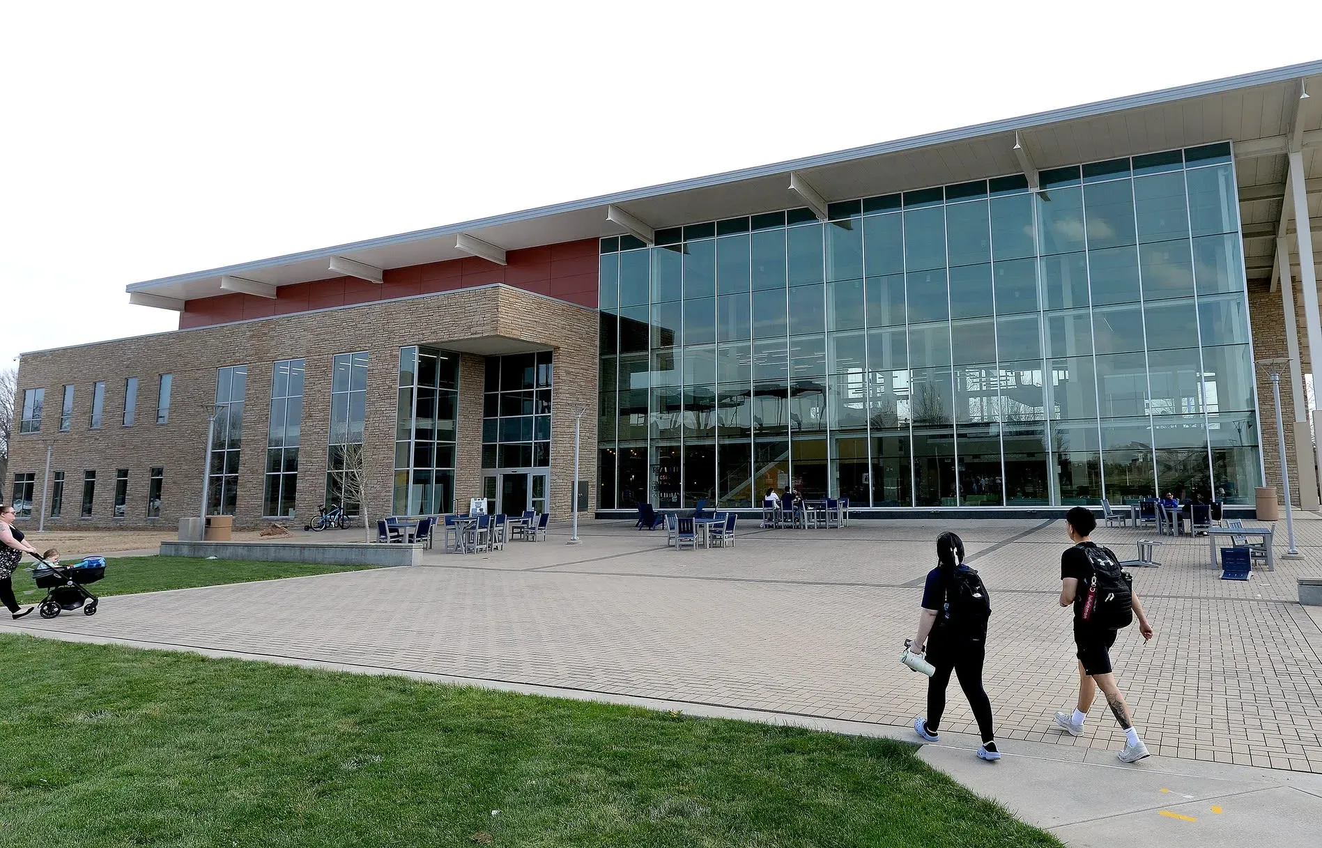 مبنى حديث يتكون من واجهة زجاجية، يظهر فيه شخصان يسيران في اتجاه المدخل. تعكس الصورة السياق الاجتماعي لقصة احتجاز Sundas Naqvi.