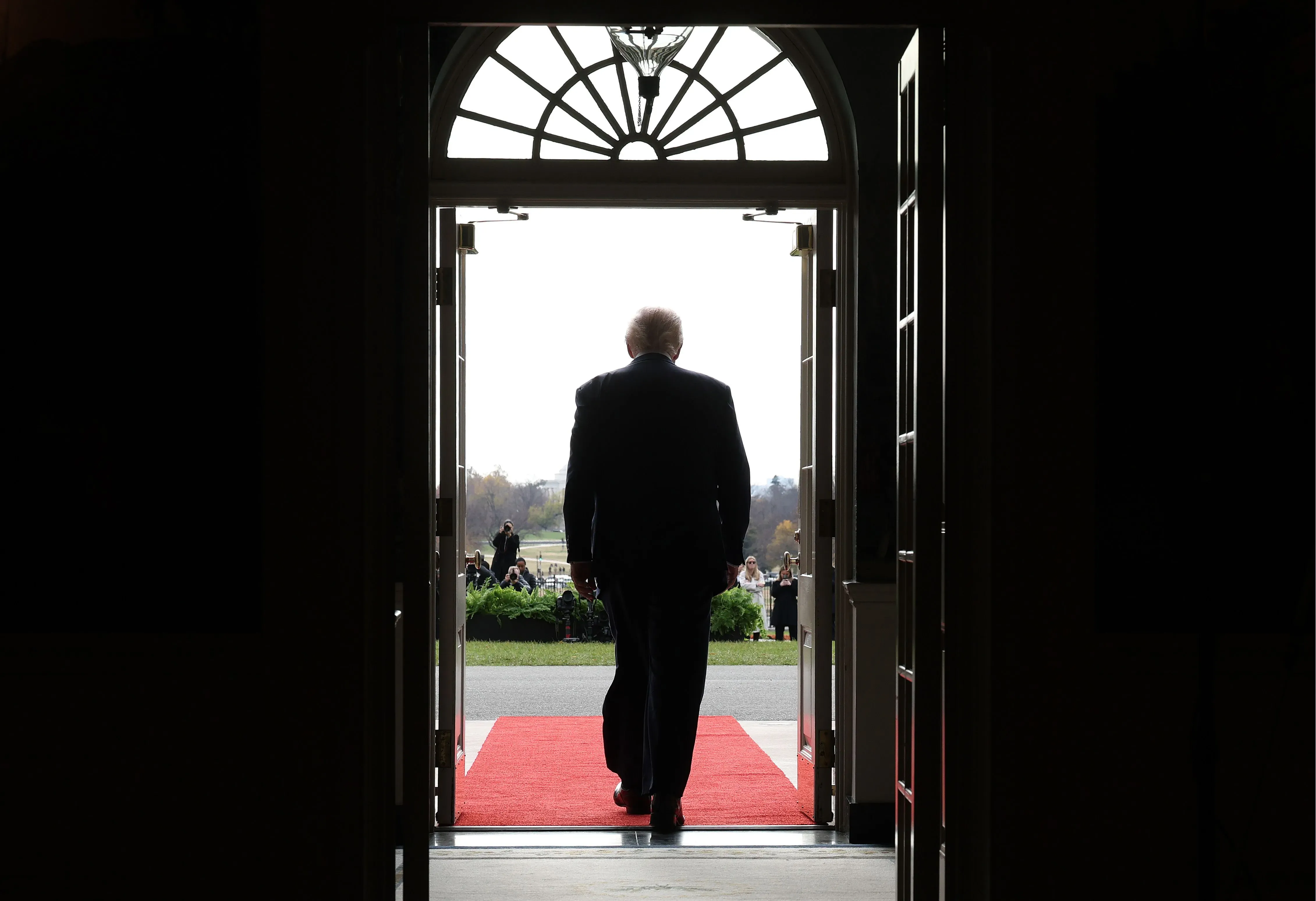 ترامب يغادر البيت الأبيض من باب مفتوح، بينما يتجمع الناس في الخارج، مما يعكس أجواء التوتر السياسي حول قضايا العدالة.