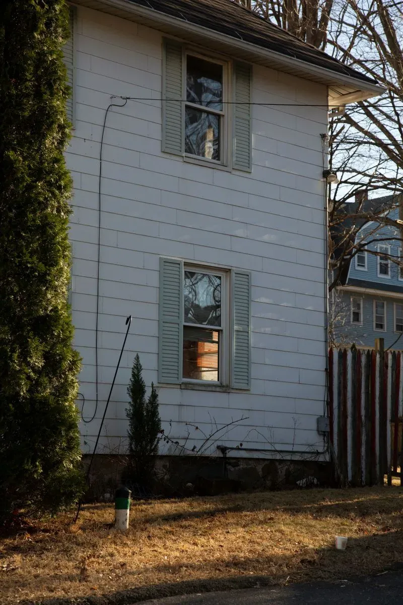 جانب من منزل مغطى بألواح خشبية في واتربري، مع نافذتين مغلقتين وأشجار قريبة، يعكس مأساة احتجاز شخص لعقود.