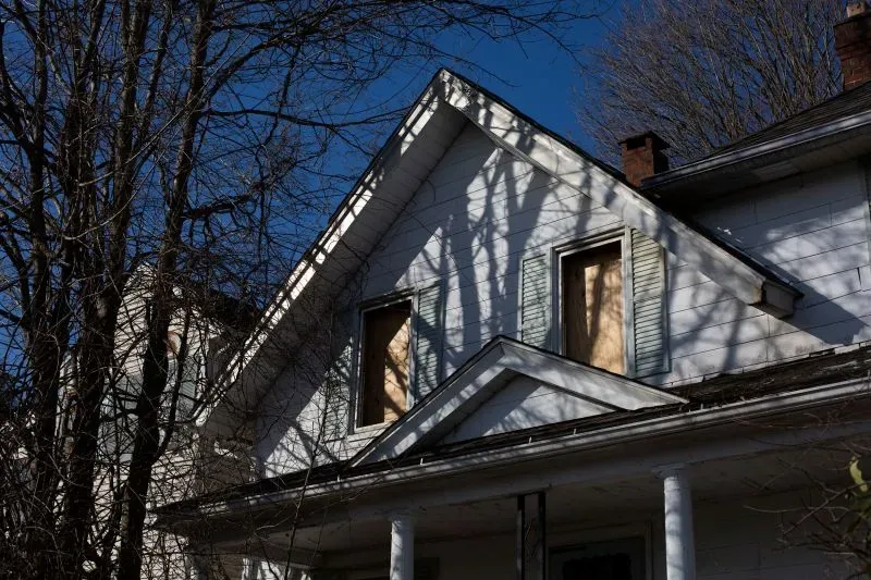 منزل مهجور في واتربري، مع نوافذ مغطاة بألواح خشبية، يتوسطه ظلال الأشجار، يشير إلى مأساة عائلية مؤلمة.