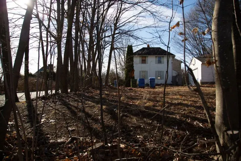 منزل أبيض قديم محاط بالأشجار، يظهر فيه صناديق زرقاء في الفناء. يُعرف المكان بـ "بيت الرعب" بعد حادثة حريق مروعة.