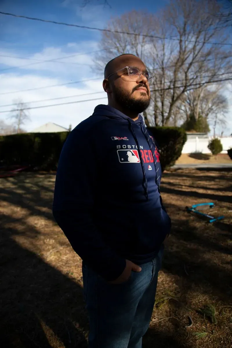 رجل يقف في حديقة أمام منزله، يتأمل في الأحداث الأخيرة المتعلقة بحادثة احتجاز في واتربري، مع أجواء هادئة تعكس التوتر في المجتمع.