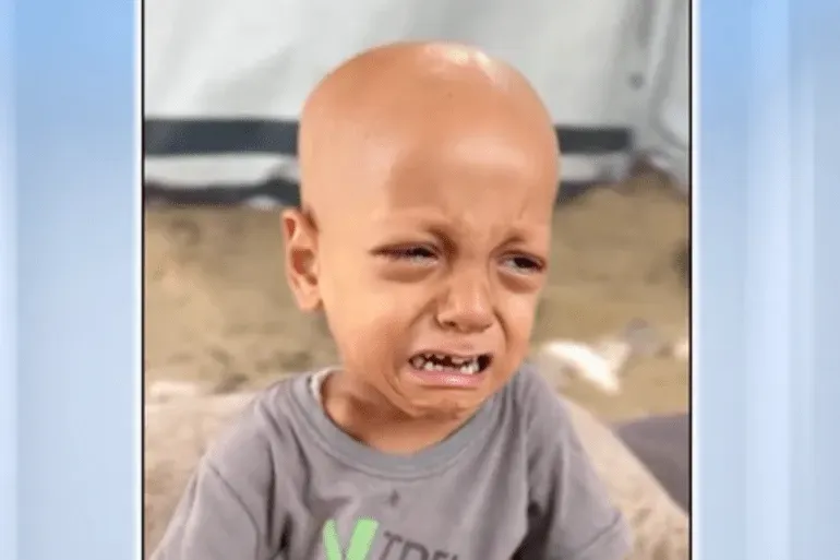 طفل صغير يبكي بعمق، يعكس معاناة سوء التغذية في غزة، يرتدي قميصًا رماديًا، ويظهر وجهه الهزيل وعيونه الكبيرة.