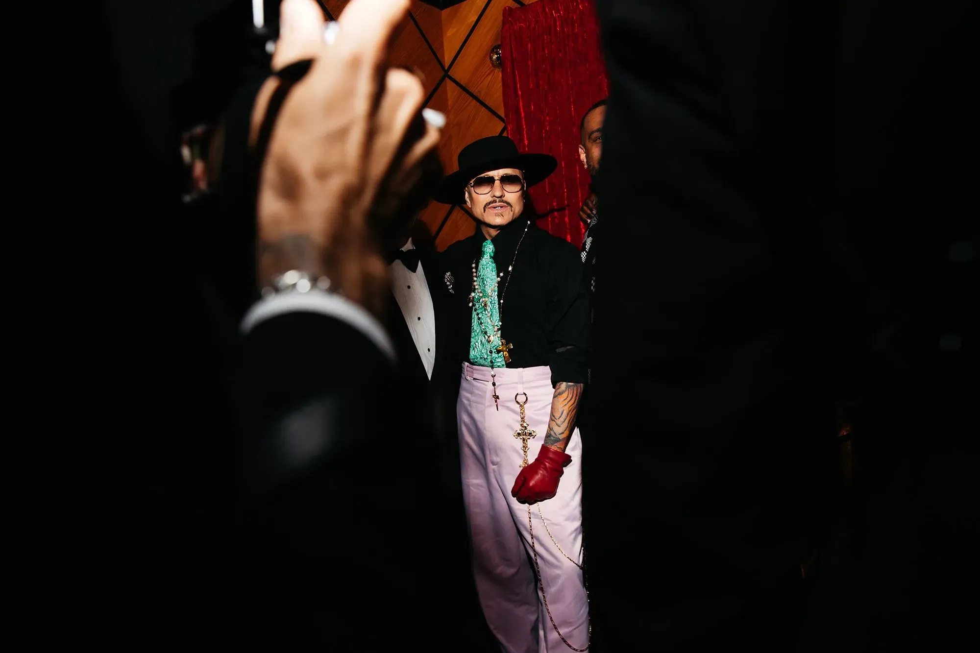 مصمم يرتدي زيًا مميزًا مع قفاز أحمر، يقف في خلفية الحدث، مع التركيز على أسلوبه الفريد وتأثير الثقافة المكسيكية.