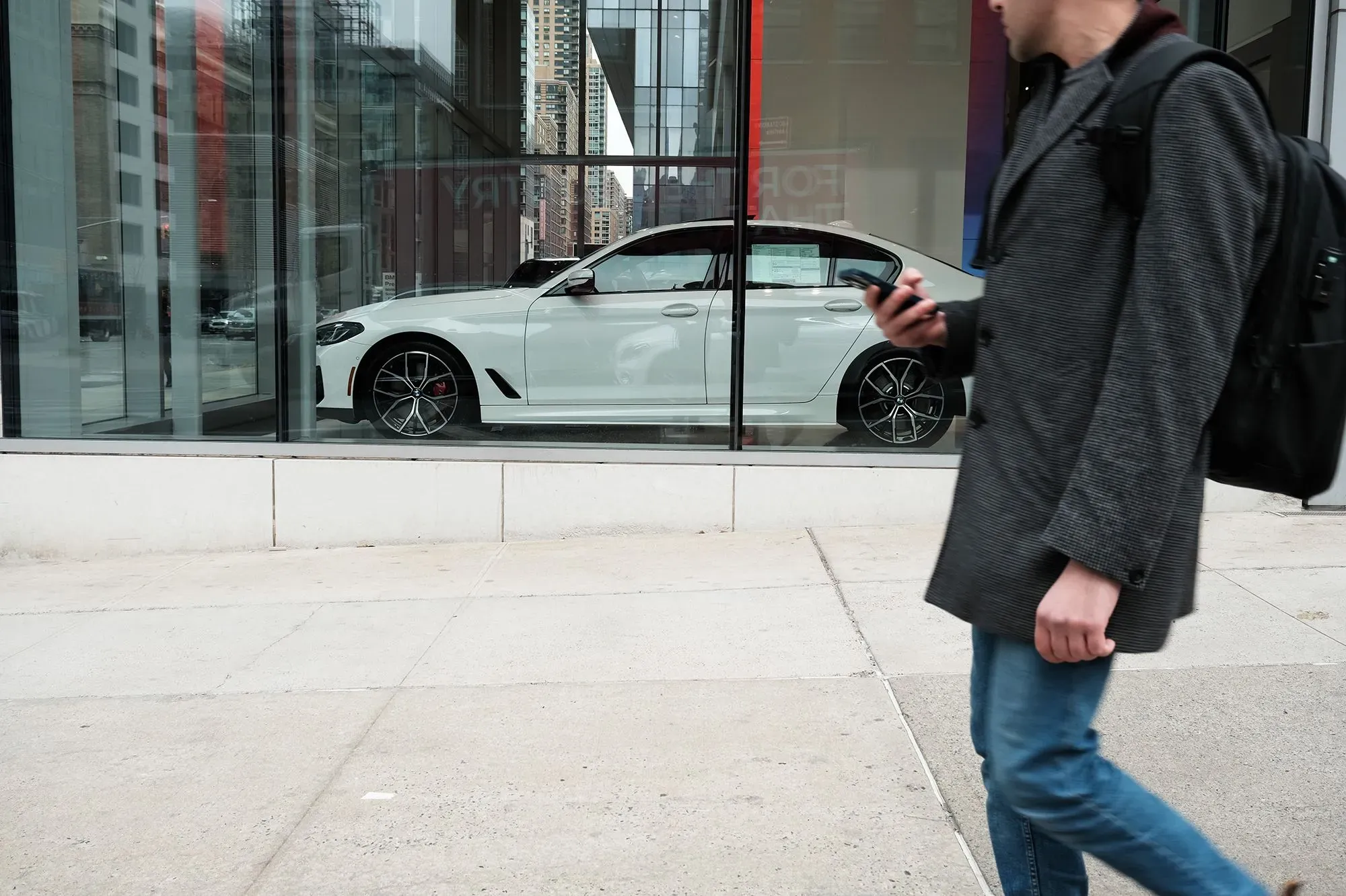 رجل يمشي بجانب واجهة عرض تحتوي على سيارة بيضاء حديثة، تعكس الضغوط المالية وارتفاع تكاليف المعيشة في الولايات المتحدة.