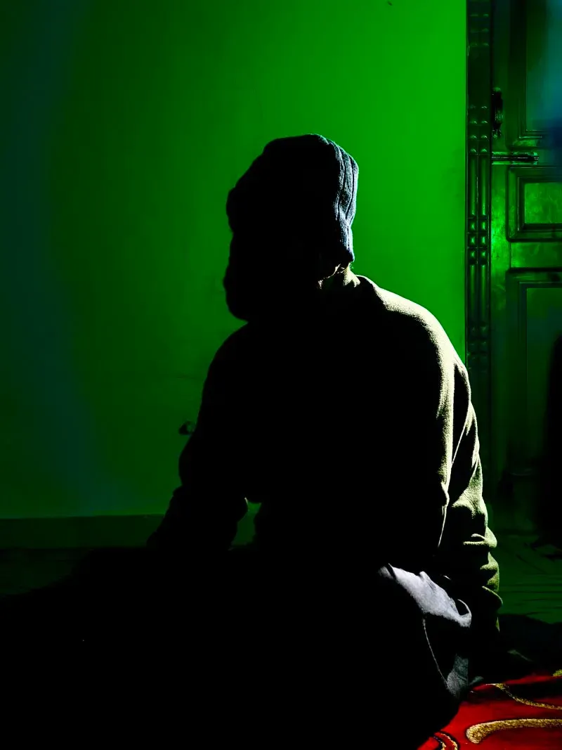 ظل شخص يجلس في غرفة مضاءة بلون أخضر، مع ملامح غير واضحة، يعكس حالة القلق والخوف بعد سيطرة طالبان على أفغانستان.
