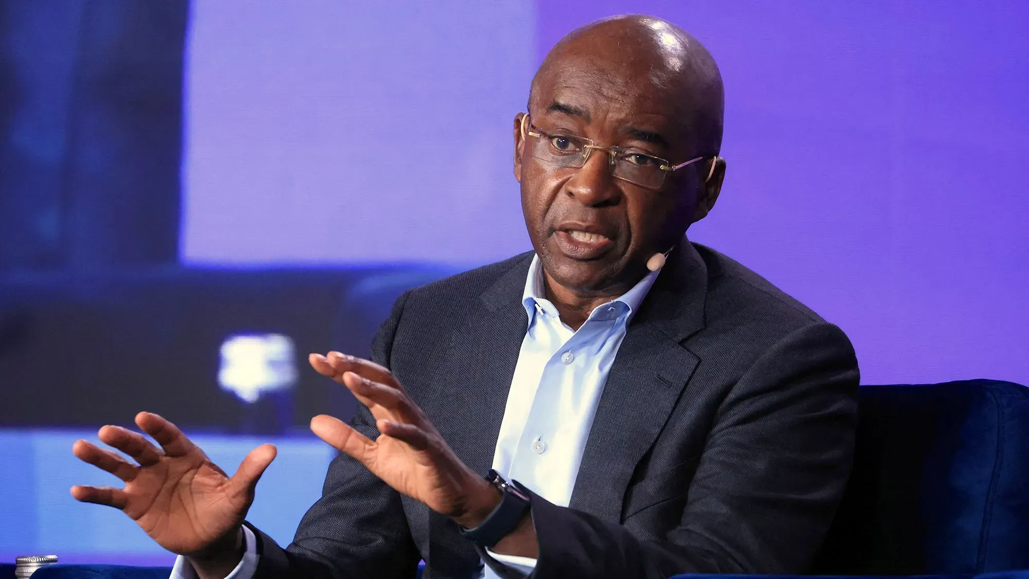 رجل أعمال يتحدث في قمة حول الذكاء الاصطناعي في كيغالي، رواندا، مع خلفية ملونة، حيث يناقش فرص الابتكار في أفريقيا.