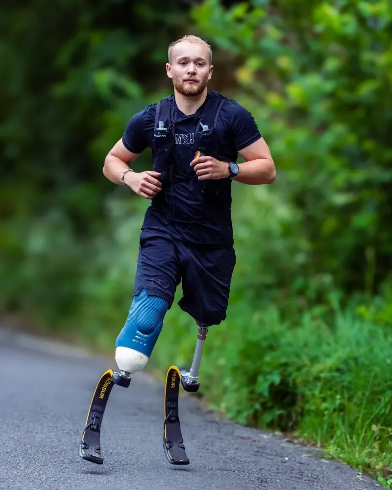 يظهر بيلي مونجر، البالغ من العمر 25 عامًا، وهو يجري على طريق محاط بالأشجار، مرتديًا أطرافًا صناعية، بعد تحطيمه الرقم القياسي العالمي في سباق الرجل الحديدي.