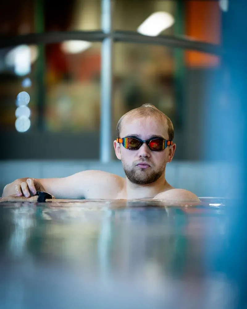 بيلي مونجر، شاب مبتور الساقين، يستعد للسباحة في مسبح، مرتديًا نظارات السباحة، مع تعبير جاد يعكس عزيمته على التغلب على التحديات.