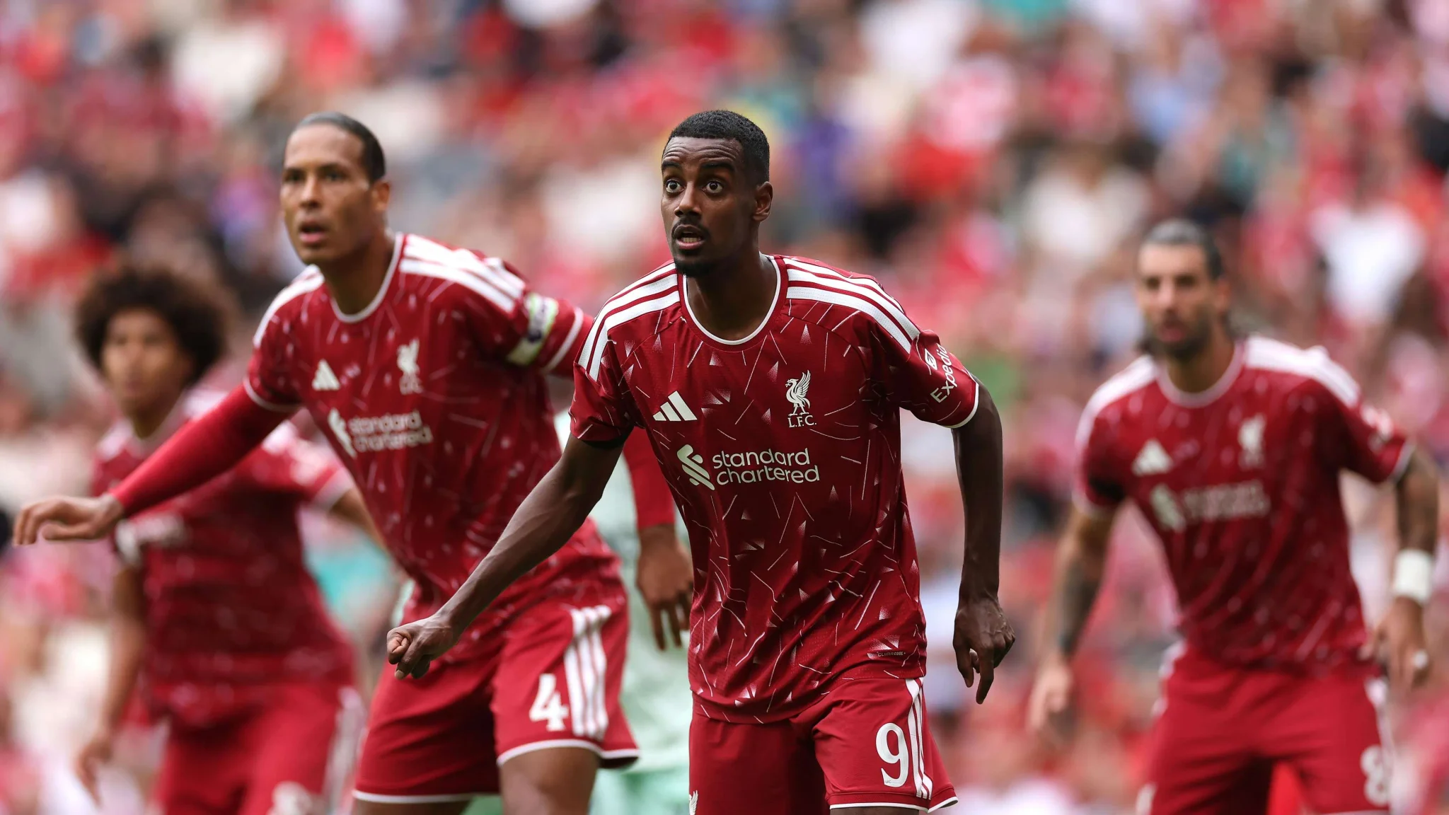 لاعبو نادي ليفربول يرتدون الزي الأحمر خلال مباراة في الدوري الإنجليزي الممتاز، مع تركيز على لاعب في المقدمة استعدادًا لتنفيذ ركلة حرة.