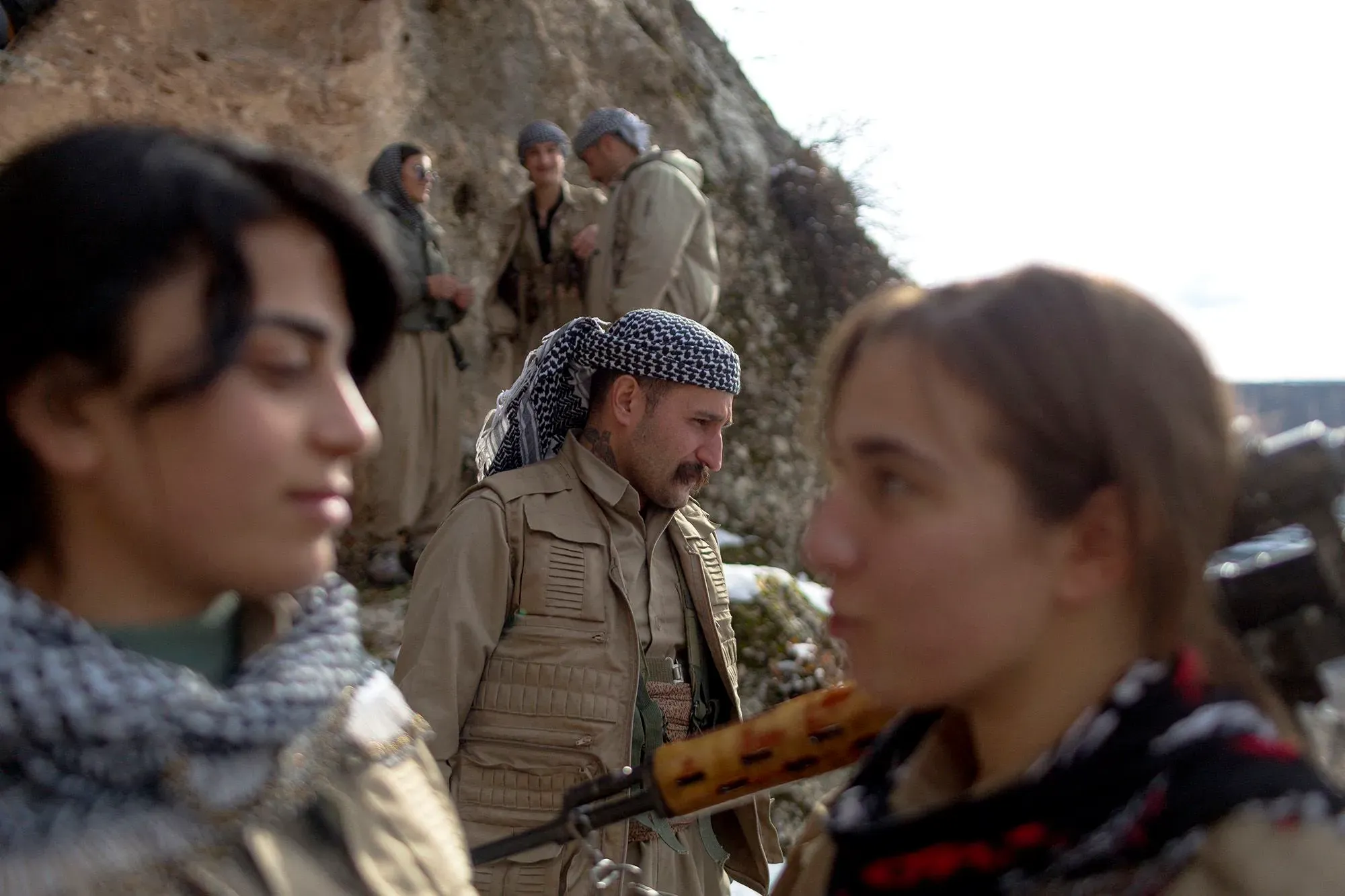 مجموعة من مقاتلي البيشمركة الكردية، بينهم شابتان تحملان أسلحة، يتبادلون الحديث في معسكر جبلي شمال شرق العراق.