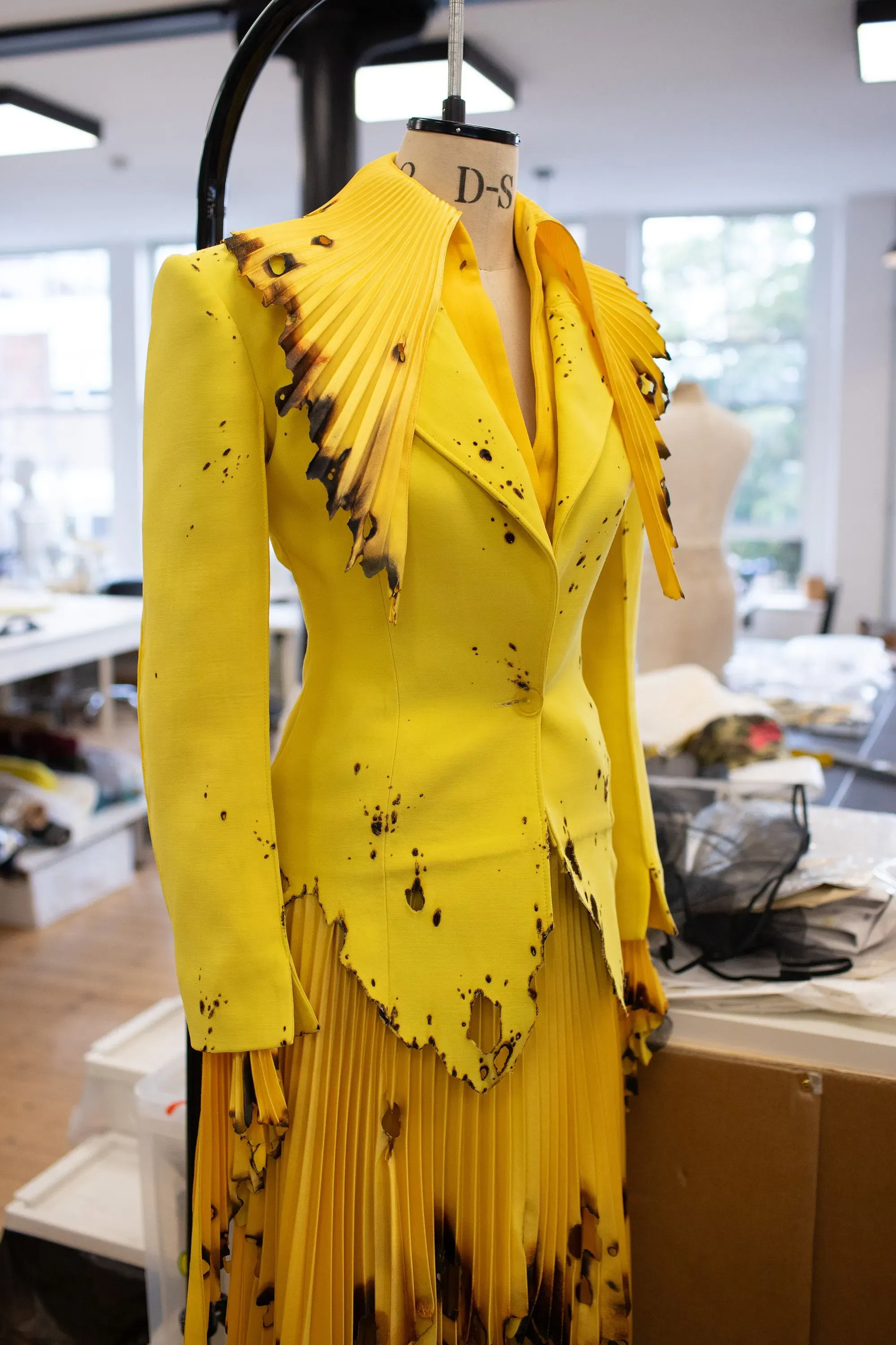 تصميم فستان أصفر مبتكر مع تفاصيل محترقة، يعكس أسلوب روبرت وون الفريد، استعدادًا لعرض أزياء في لندن.