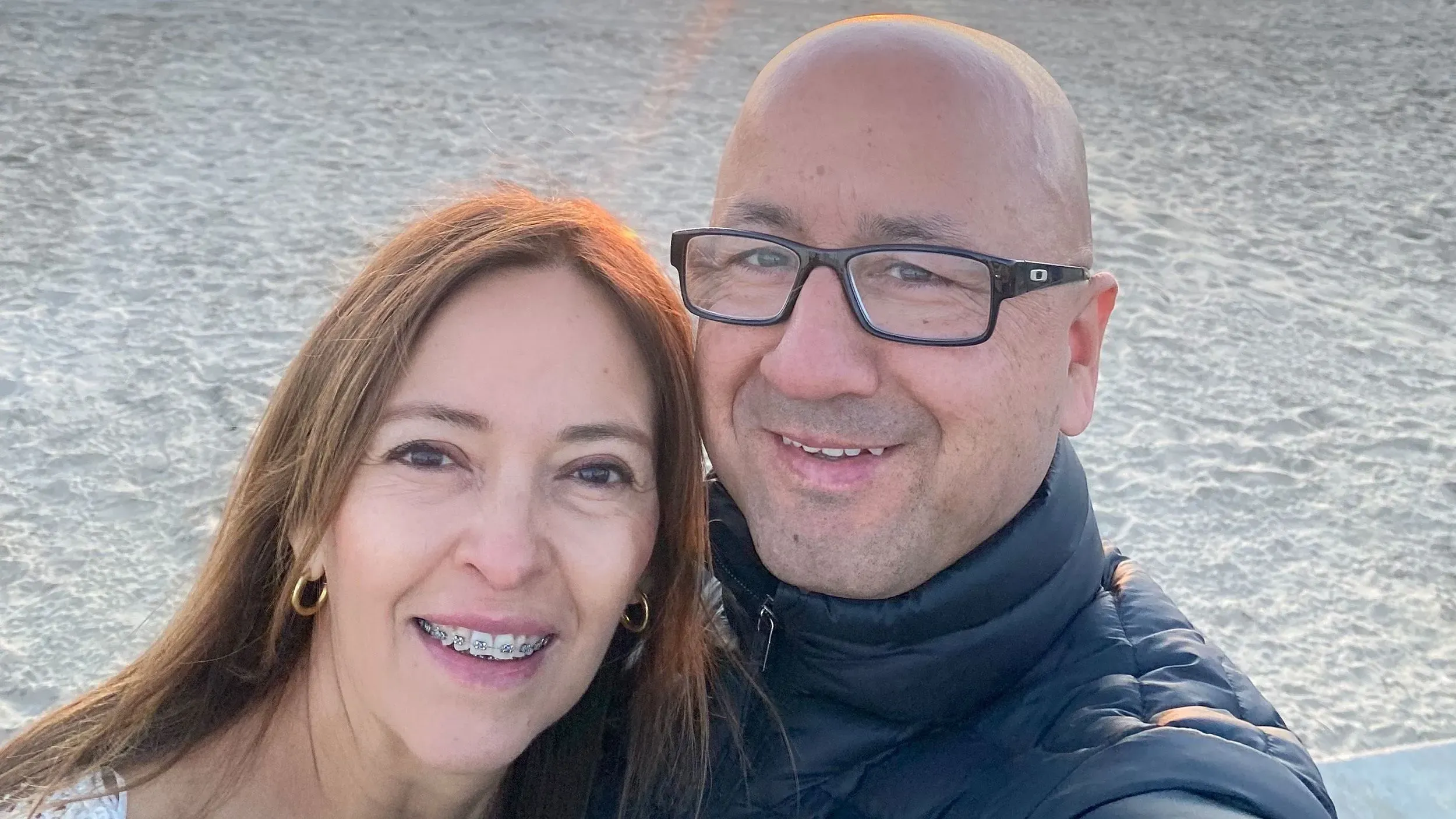 صورة لغلاديس ونيلسون غونزاليس، زوجين من كولومبيا، يبتسمان معًا على شاطئ. يعكسان قصة نضالهما في الهجرة إلى الولايات المتحدة.