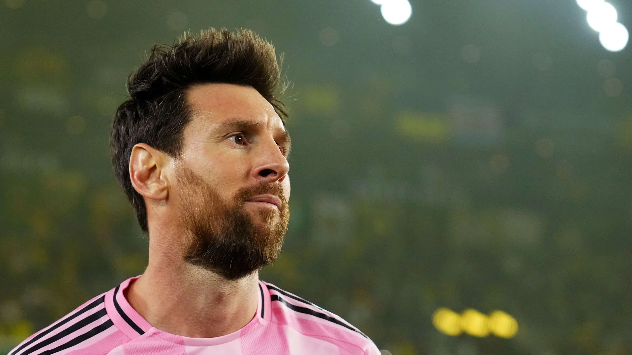 ليونيل ميسي يرتدي زي إنتر ميامي الوردي خلال مباراة، مع تركيز على وجهه وتعبيره الجاد في ملعب مضاء، في سياق مسيرته الرياضية والاستثمارية.