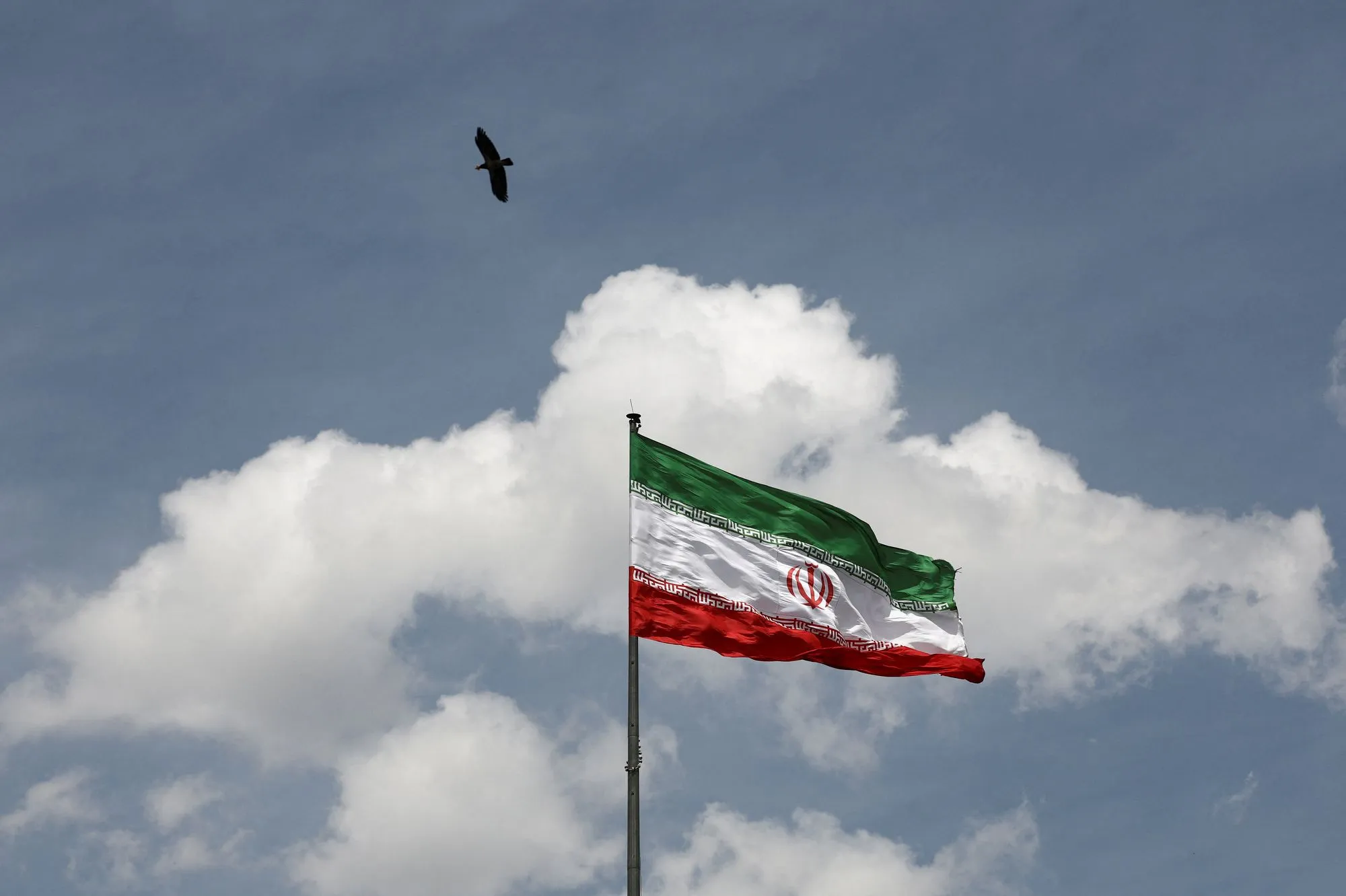 علم إيران يرفرف في السماء مع غيوم، في سياق النزاع بين إيران والولايات المتحدة حول استهداف مراكز بيانات الذكاء الاصطناعي في الخليج.
