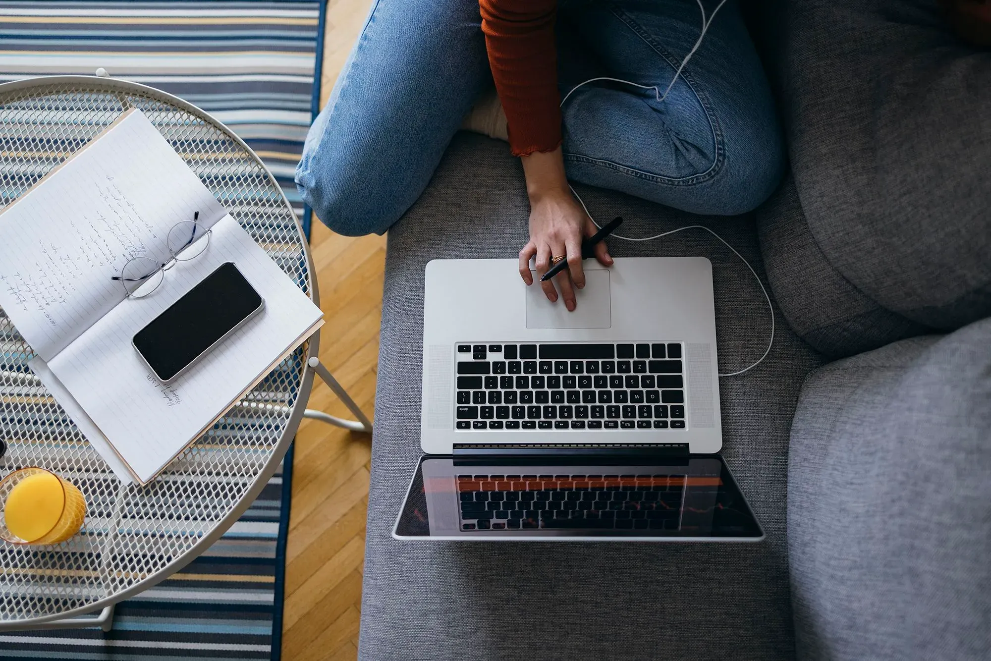 امرأة تستخدم الكمبيوتر المحمول في غرفة معيشة مريحة، محاطة بدفتر ملاحظات وهاتف ذكي، تعكس مشهد العمل عن بُعد.