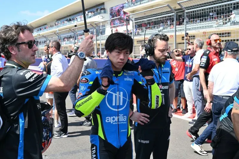 آي أوغورا، متسابق موتو جي بي، يستعد للسباق مع فريق تراكهاوس، مرتديًا زيه الرسمي، وسط أجواء حماسية في الحلبة.