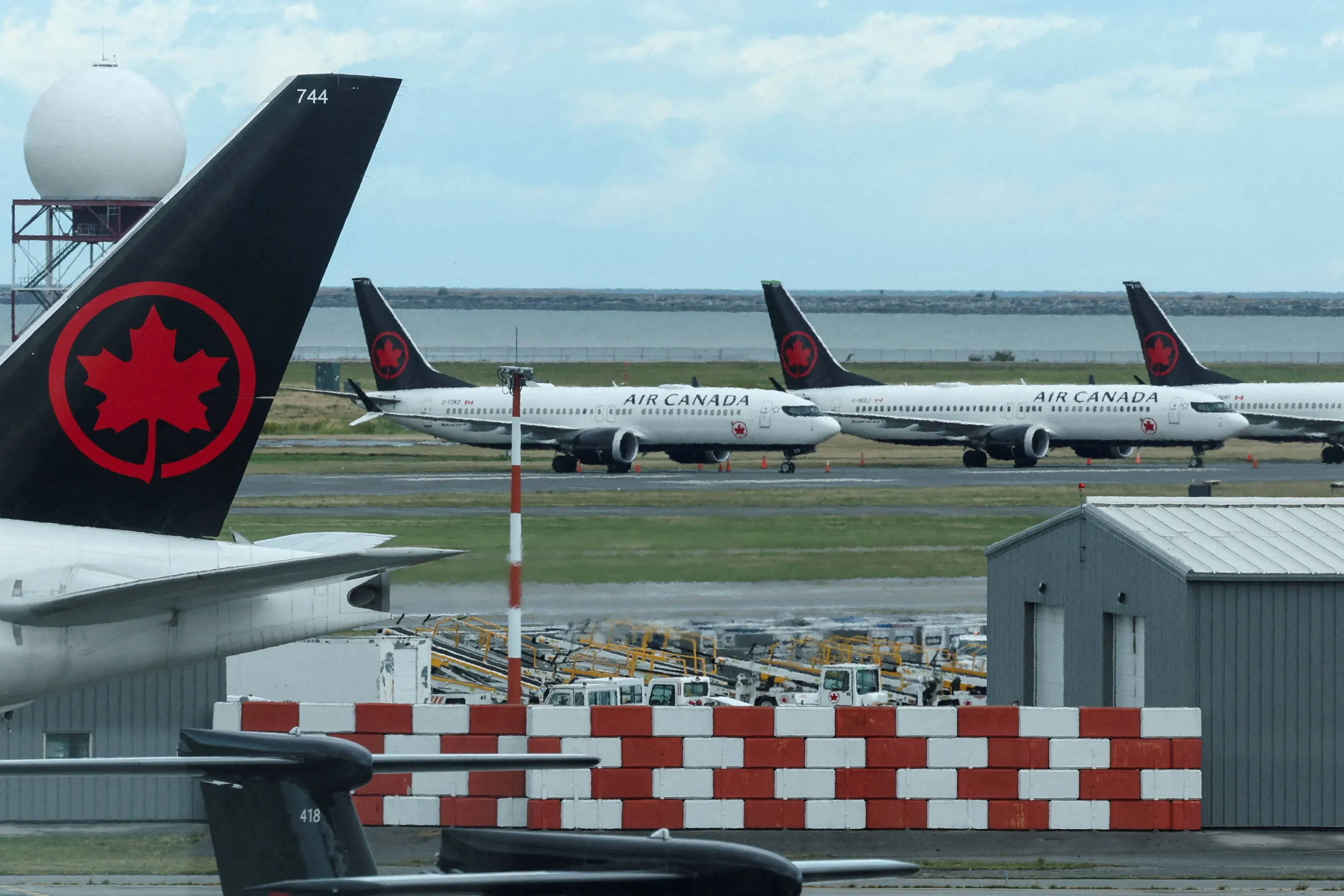 طائرات الخطوط الجوية الكندية متوقفة في المطار، مع وجود طائرة أخرى على المدرج، مما يعكس تأثير الإضراب على الرحلات الجوية.