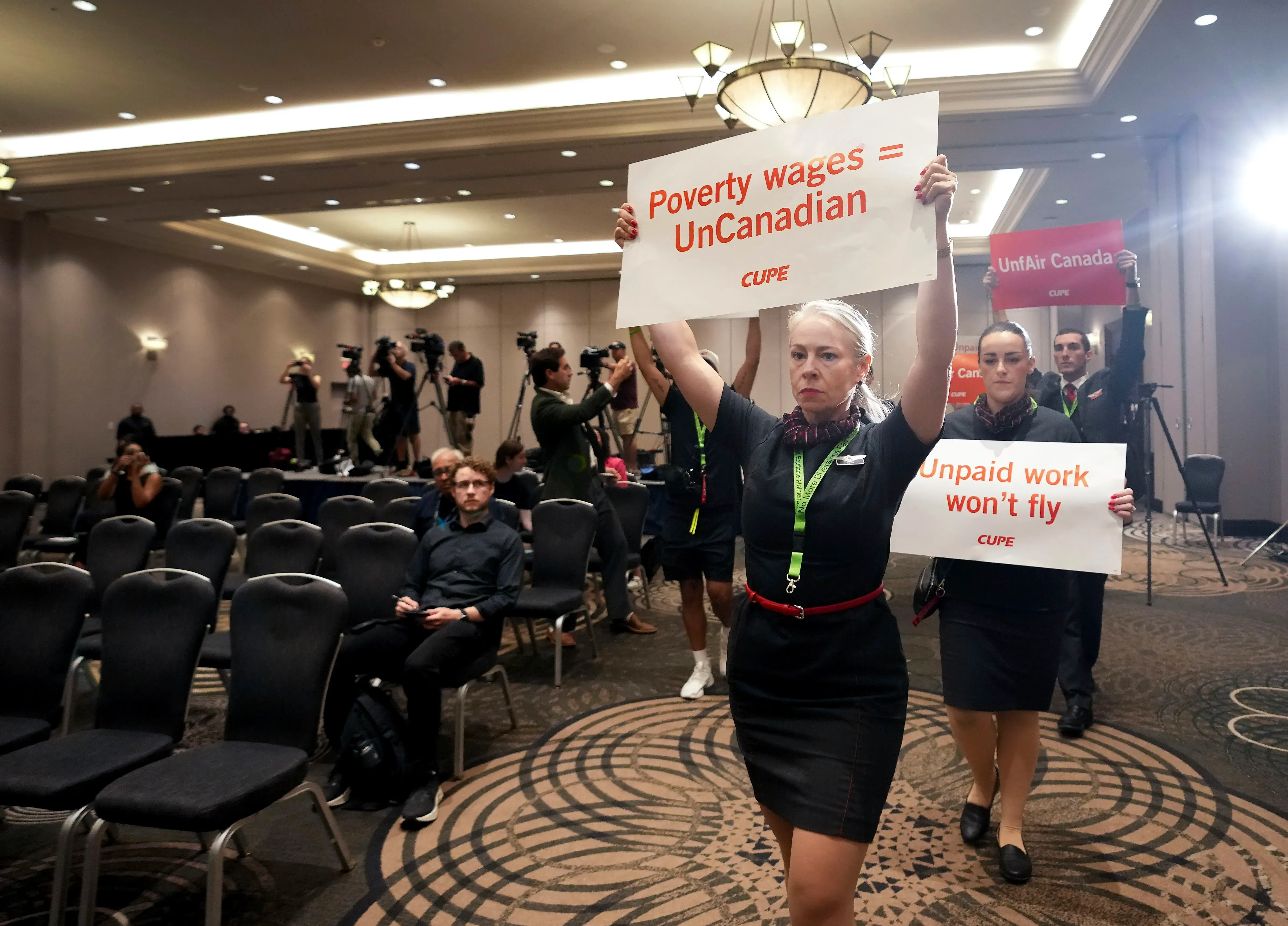 أعضاء نقابة مضيفي الخطوط الجوية الكندية يحتجون أثناء مؤتمر صحفي، حاملين لافتات تعبر عن مطالبهم حول الرواتب وظروف العمل.