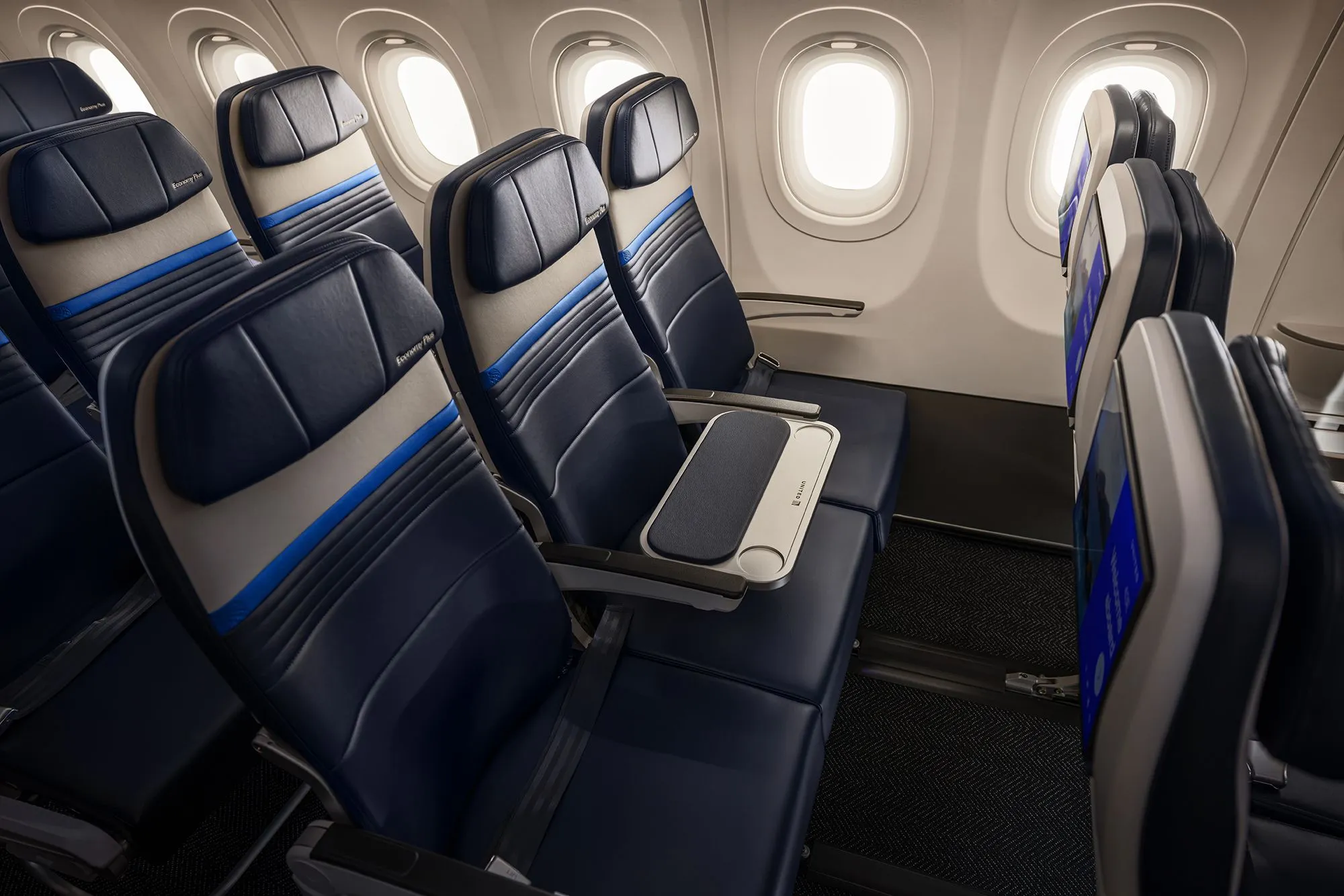 مقاعد طائرة United Airlines في قسم economy plus مع مساحة إضافية للمرفقين وطاولة وسطى محجوبة لتحسين راحة الركاب.