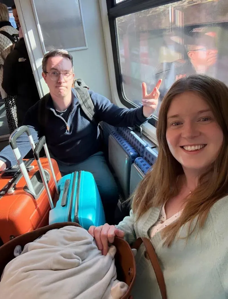 زوجان يجلسان في قطار بعد تحويل رحلتهم من لندن إلى فرانكفورت بسبب إغلاق مطار هيثرو، مع حقائبهم في الخلفية.