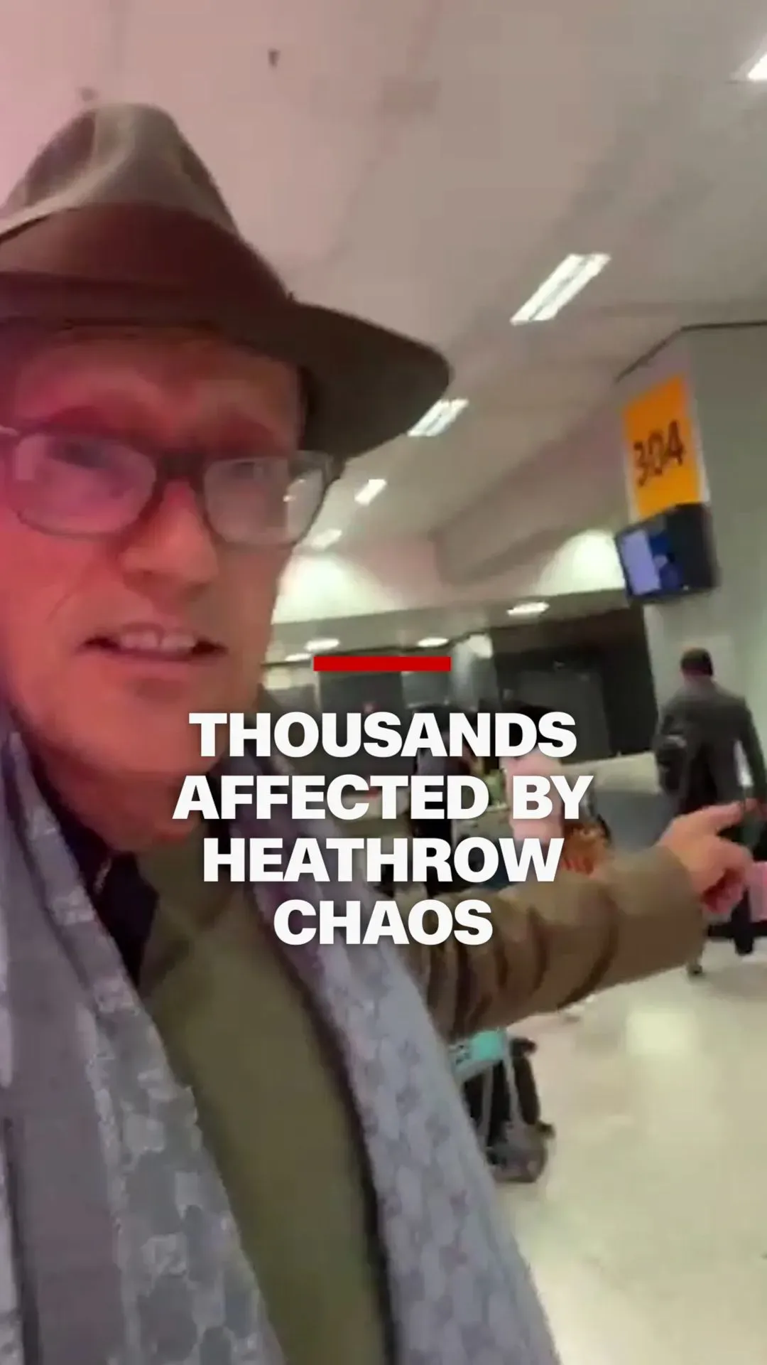 رجل يرتدي قبعة يوجه كاميرا الهاتف نحو المطار، مع وجود لافتة تشير إلى الاضطراب في مطار هيثرو وتأثيره على آلاف المسافرين.