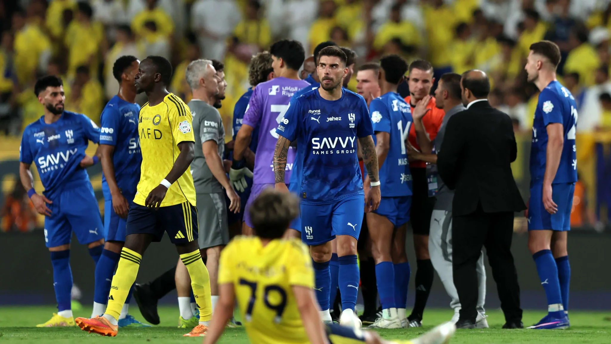 لاعبو الهلال بالزي الأزرق يتفاعلون في مباراة حاسمة ضد فريق النصر بالزي الأصفر ضمن منافسات الدوري السعودي للمحترفين.