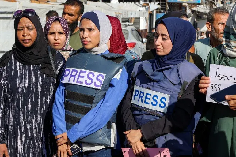 مجموعة من الصحفيين في غزة يرتدون سترات تحمل كلمة "PRESS"، يعبرون عن معاناتهم ويدعون لوقف التجويع القسري والاعتداءات.