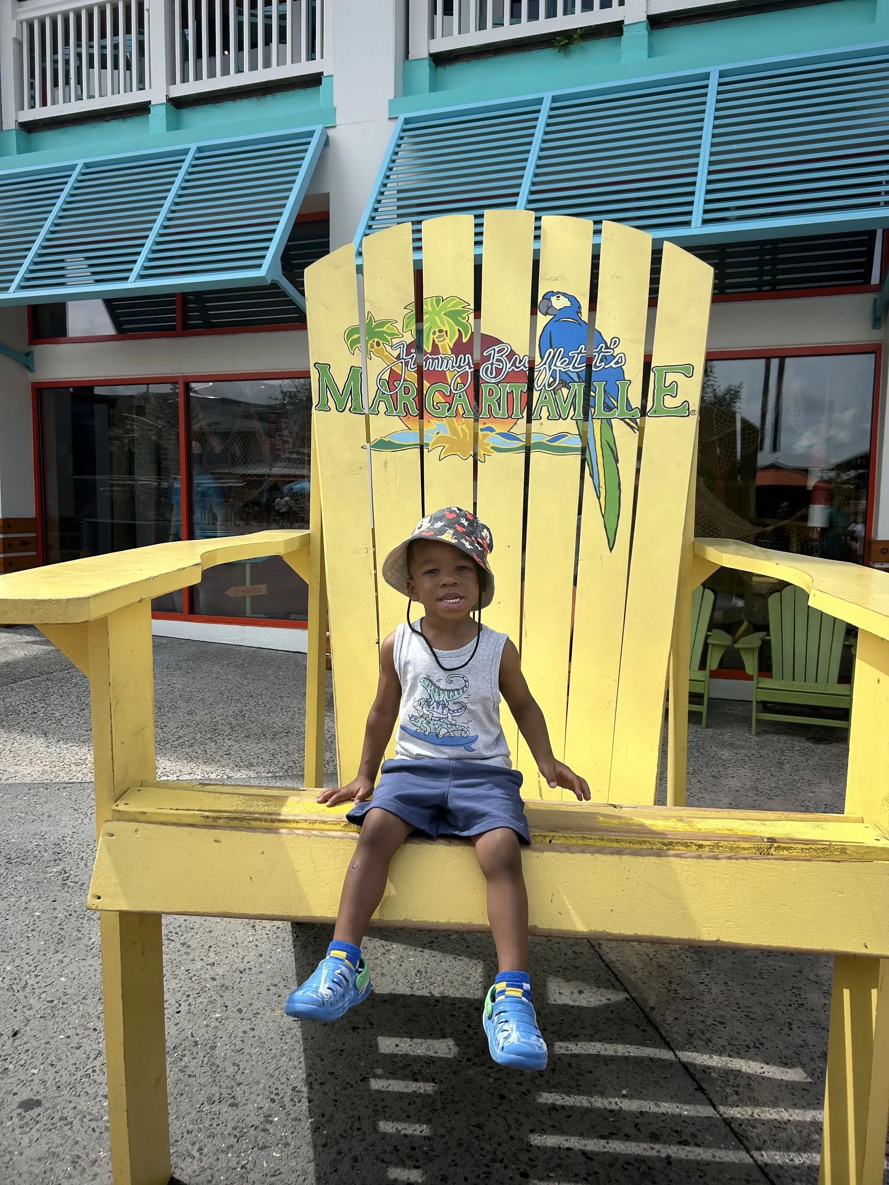 طفل صغير يجلس مبتسمًا على كرسي أصفر كبير في منطقة ترفيهية، يعكس روح المرح والسعادة التي تميز شخصيته.