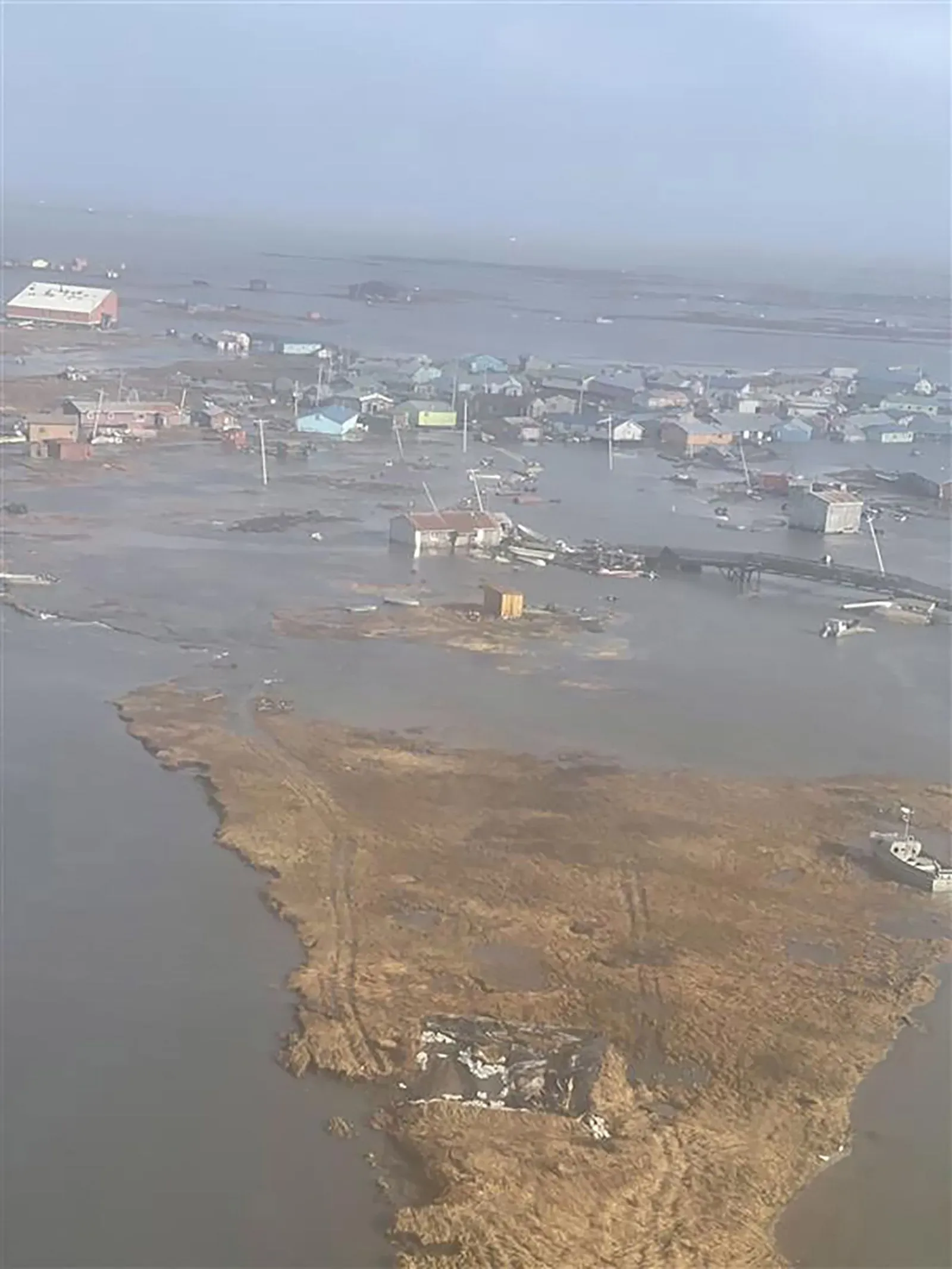 تظهر الصورة مشهدًا جويًا لمجتمعات ساحلية في ألاسكا غمرتها المياه بعد إعصار هالونج، مع منازل مدمرة وأراضٍ مغمورة.