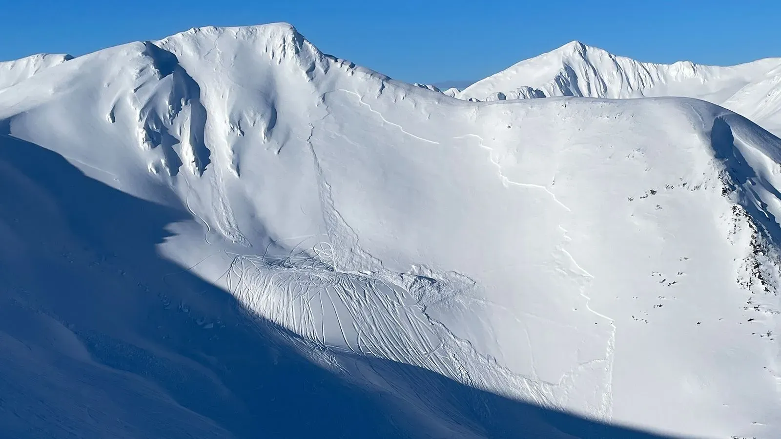 منحدر ثلجي في ألاسكا يظهر آثار انهيار جليدي مع مسارات تزلج، مما يعكس الظروف الخطرة التي أدت إلى حوادث مميتة.