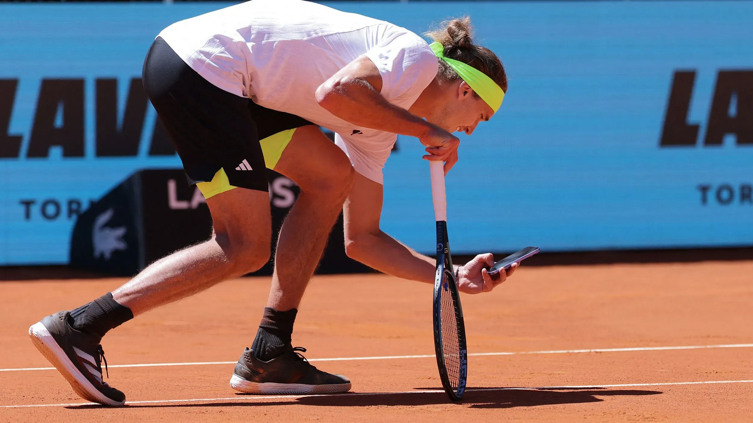 أليكس زفيريف ينحني لالتقاط صورة بهاتفه لعلامة كرة متنازع عليها خلال مباراة تنس على الملاعب الرملية، معبرة عن الجدل حول استخدام نظام الحكم الإلكتروني.