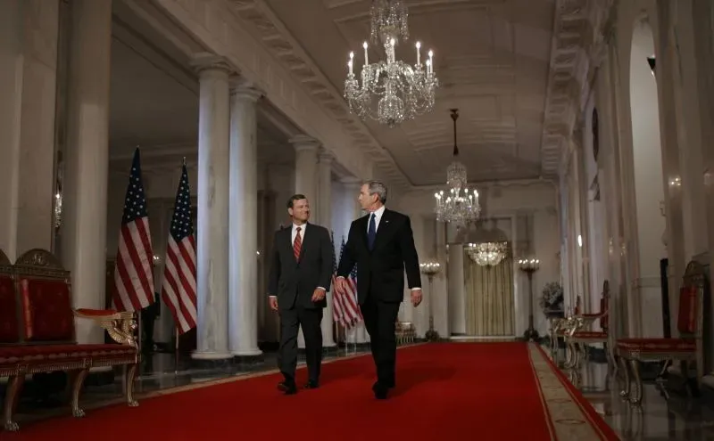 رئيس المحكمة العليا جون روبرتس والقاضي صامويل أليتو يسيران معًا في قاعة مزينة بأعلام أمريكية وثريات، مع التركيز على التقاعد والتغييرات المحتملة في المحكمة.