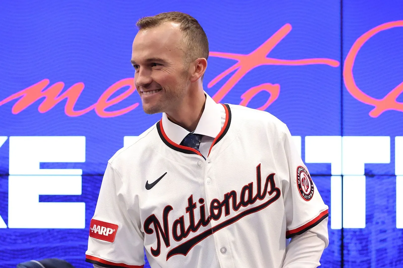 بليك بوتيرا مبتسم في مؤتمر تقديمه كمدير جديد لفريق واشنطن ناشونالز، مرتديًا قميص الفريق، مع خلفية تحمل اسم الفريق.