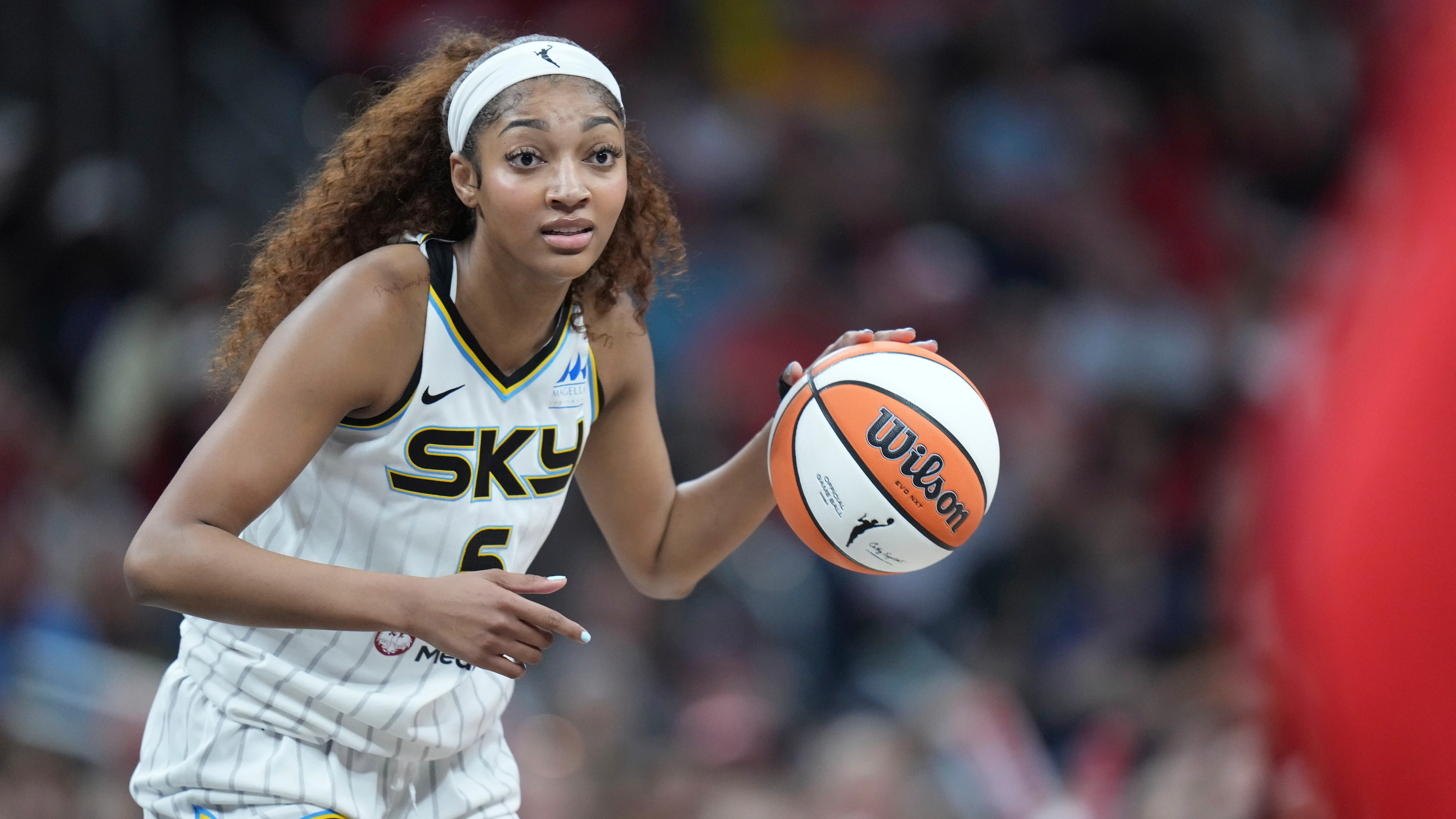 لاعبة كرة السلة أنجيل ريس من فريق شيكاغو سكاي تحمل الكرة وتستعد للتمرير خلال مباراة، مع أجواء حماسية في الملعب.