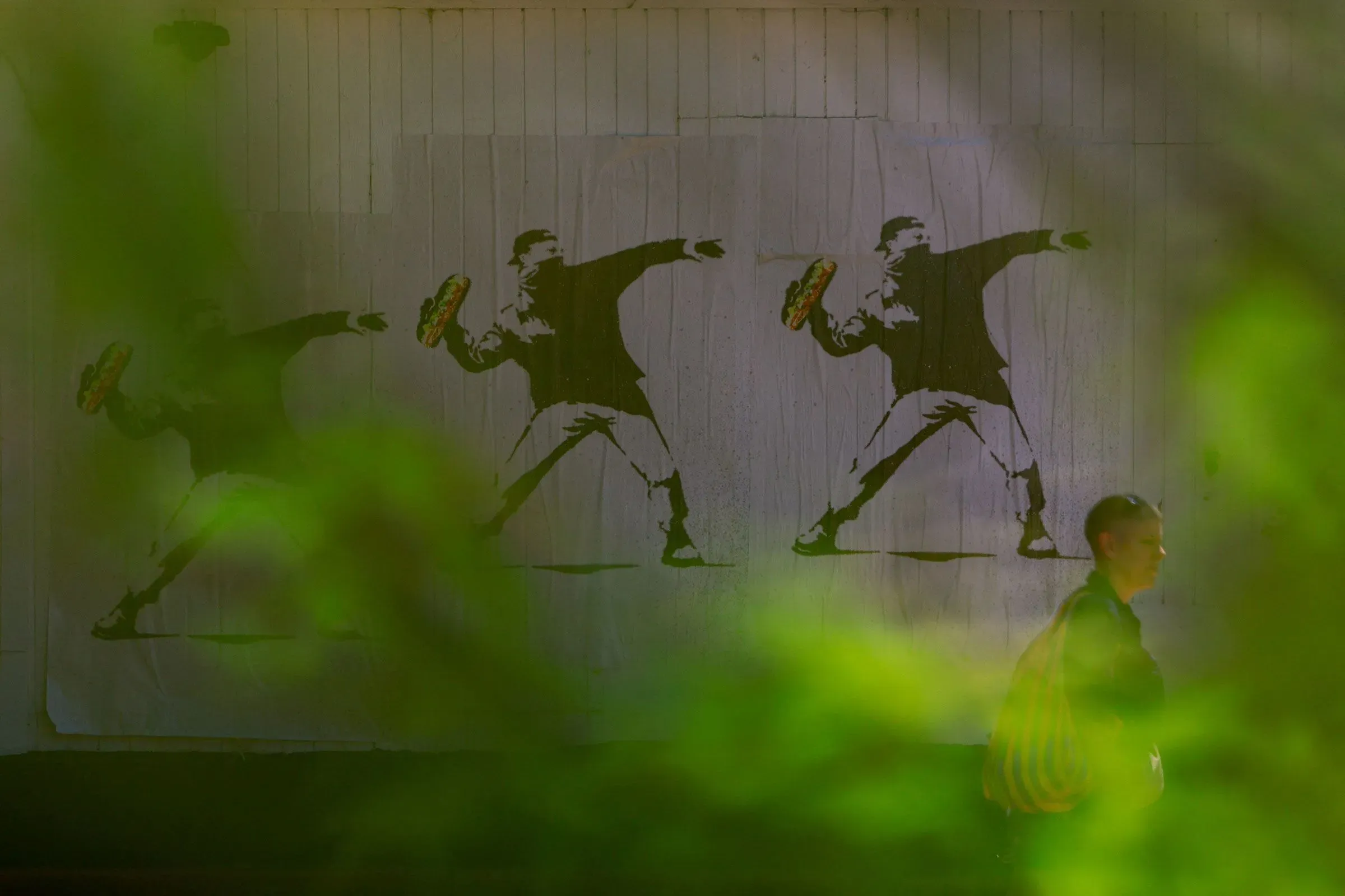 رجل يسير بجانب جدارية تُظهر شخصًا يلقي بشطيرة، تعبيرًا عن الاحتجاج، في سياق قضية جنائية في واشنطن.