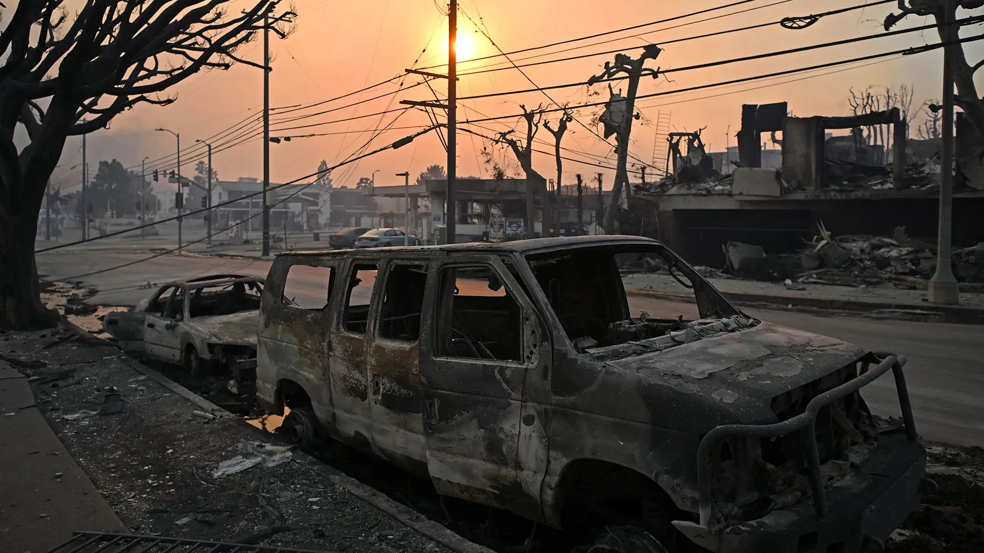 حرائق الغابات في كاليفورنيا تسببت في تدمير سيارات ومنازل، مع شروق الشمس في الخلفية، مما يعكس آثار الكارثة.