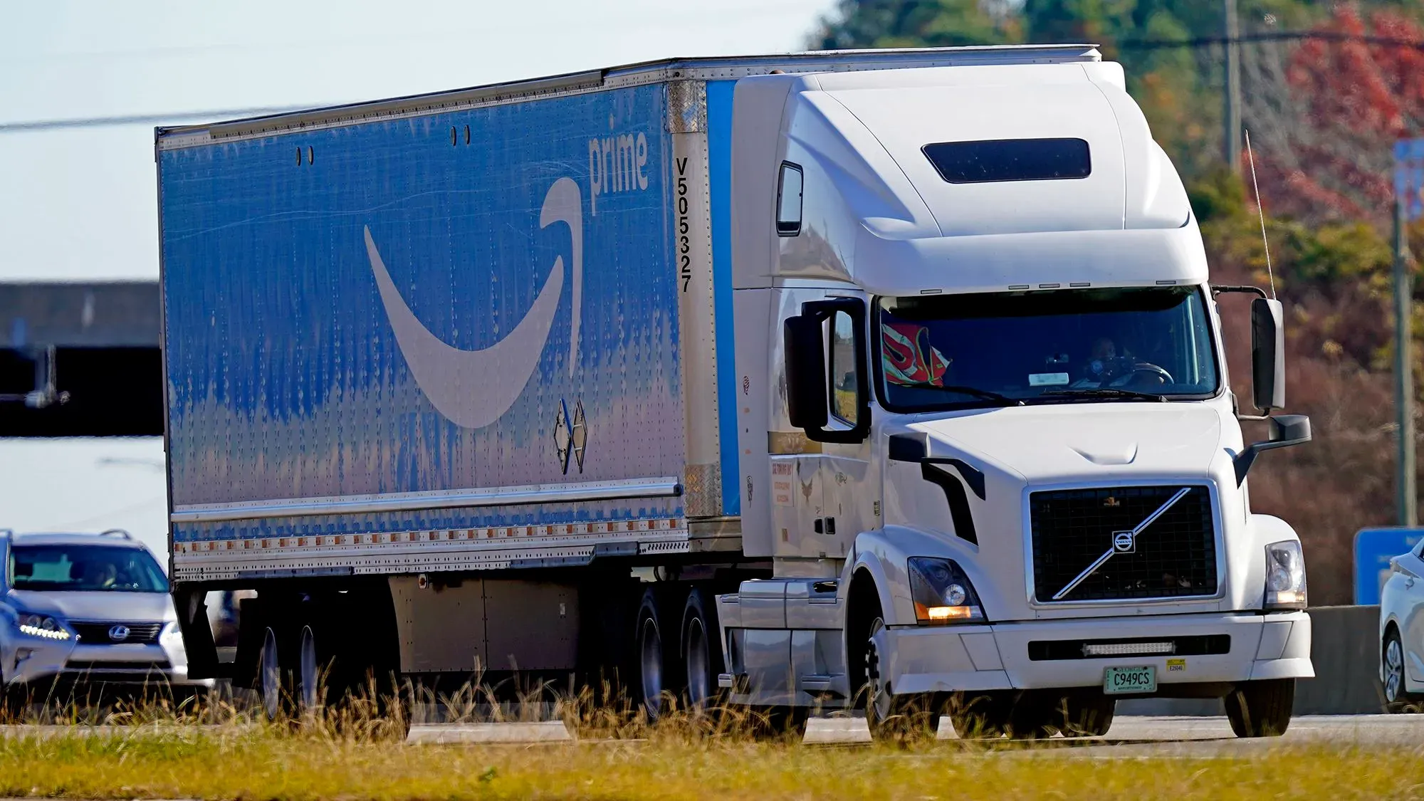 شاحنة توصيل تابعة لأمازون تحمل شعار "برايم" تسير على طريق سريع، تعكس جهود الشركة في مجال التوصيل والنقل.