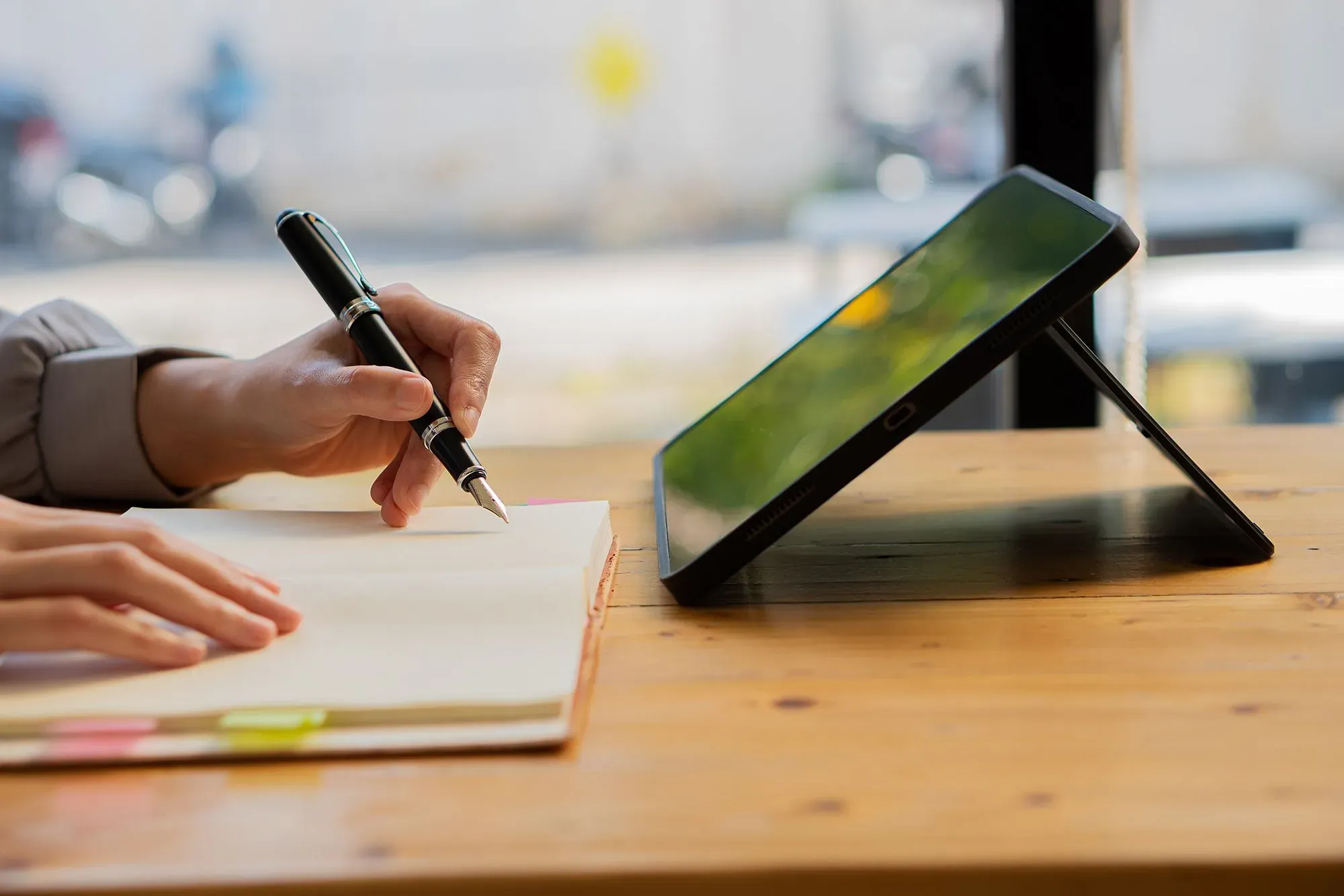 يد عازف يكتب في دفتر ملاحظات بينما يستند جهاز لوحي على الطاولة، مما يعكس استخدام التكنولوجيا في التعليم.