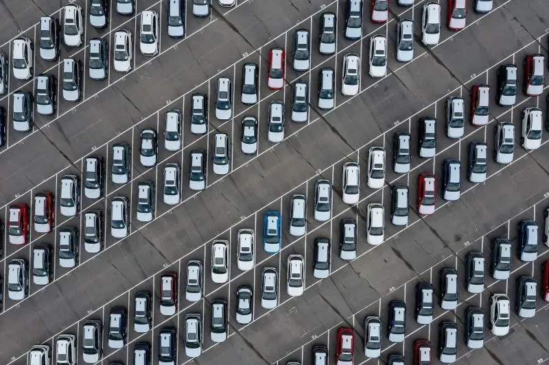 صورة تظهر صفوفًا منظمة من السيارات في موقف سيارات واسع، مع وجود سيارة زرقاء مميزة بين السيارات البيضاء والفضية.