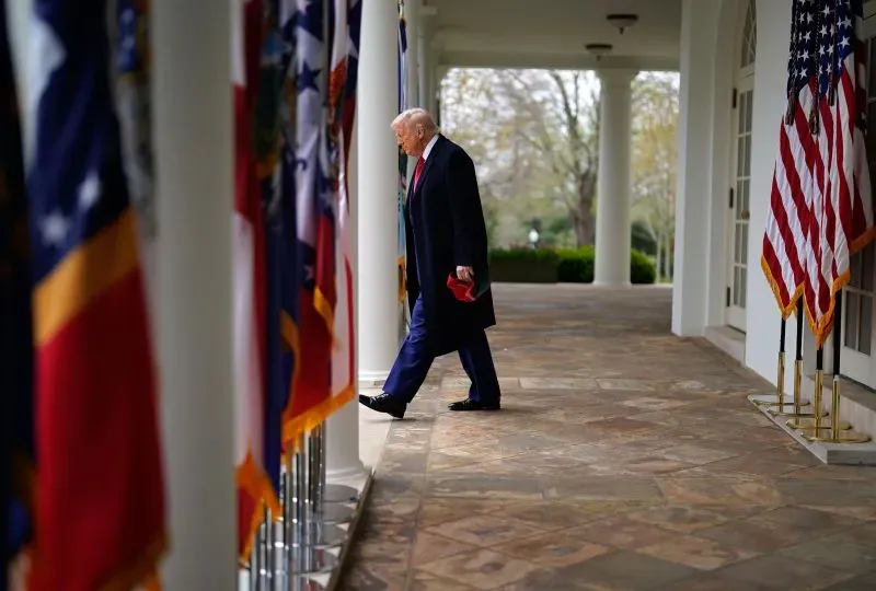 ترامب يسير في ممر البيت الأبيض محاطًا بالأعلام، معبرًا عن ثقته في استراتيجيته التجارية الجديدة وتأثيرها على الاقتصاد الأمريكي.