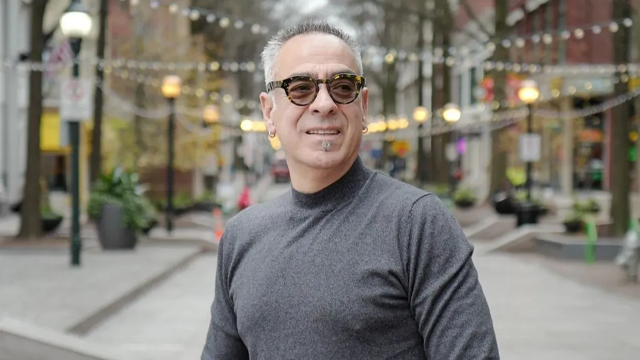 جورج غليزمان، المواطن الأمريكي الذي أُطلق سراحه بعد عامين في أفغانستان، يظهر مبتسمًا في شارع مزدحم، مع أضواء في الخلفية.