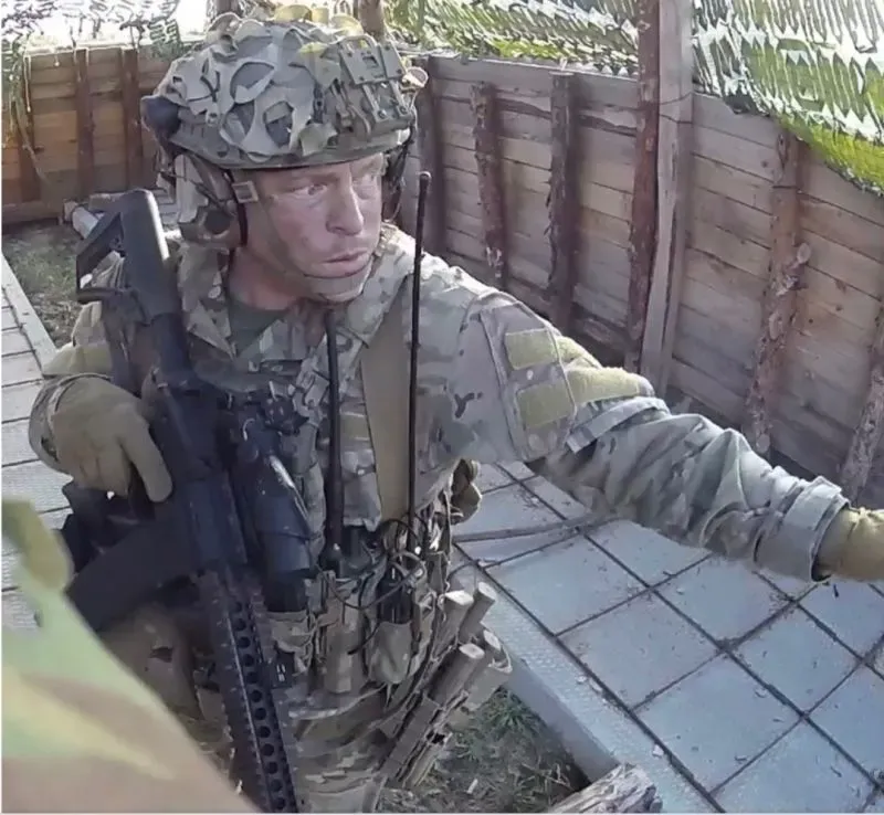 مقاتل في الجيش الأوكراني يرتدي خوذة ودرعًا، يجلس في موضع دفاعي، مع أسلحة ومعدات عسكرية حوله، في خندق على الخطوط الأمامية.