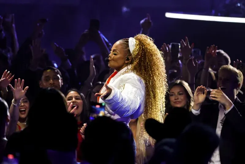 جانيت جاكسون تؤدي على المسرح في حفل توزيع جوائز الموسيقى الأمريكية، مع تفاعل حماسي من الجمهور حولها.