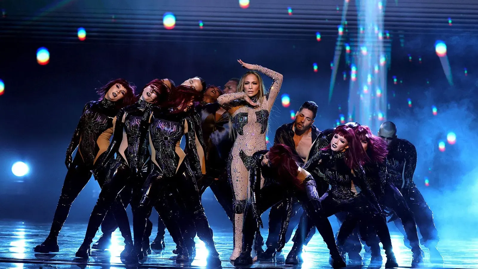 أداء راقص لجينيفر لوبيز مع مجموعة من الراقصين خلال حفل توزيع جوائز الموسيقى الأمريكية، مع أضواء ملونة خلفهم.