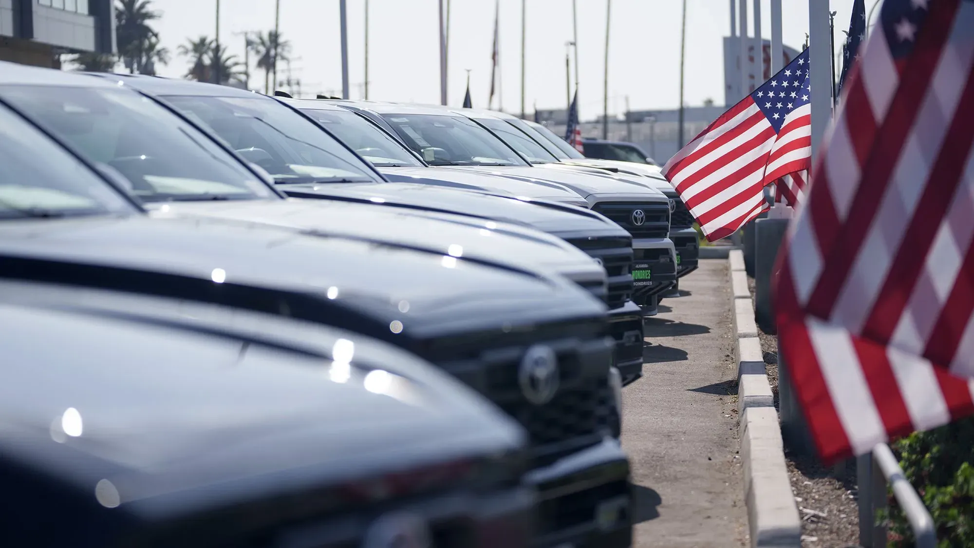 صف من السيارات السوداء في معرض سيارات أمريكي، مع أعلام الولايات المتحدة تتمايل في الخلفية، تعكس زيادة في قروض السيارات والديون.