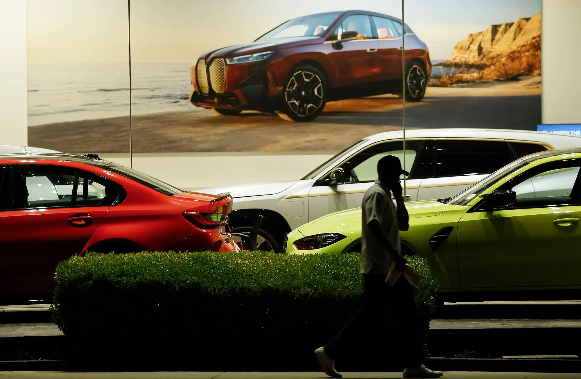 صورة تعرض مجموعة من السيارات الجديدة في معرض، مع شخص يمشي بجانبها، مما يبرز أزمة القدرة على تحمل تكاليف السيارات في السوق الأمريكية.