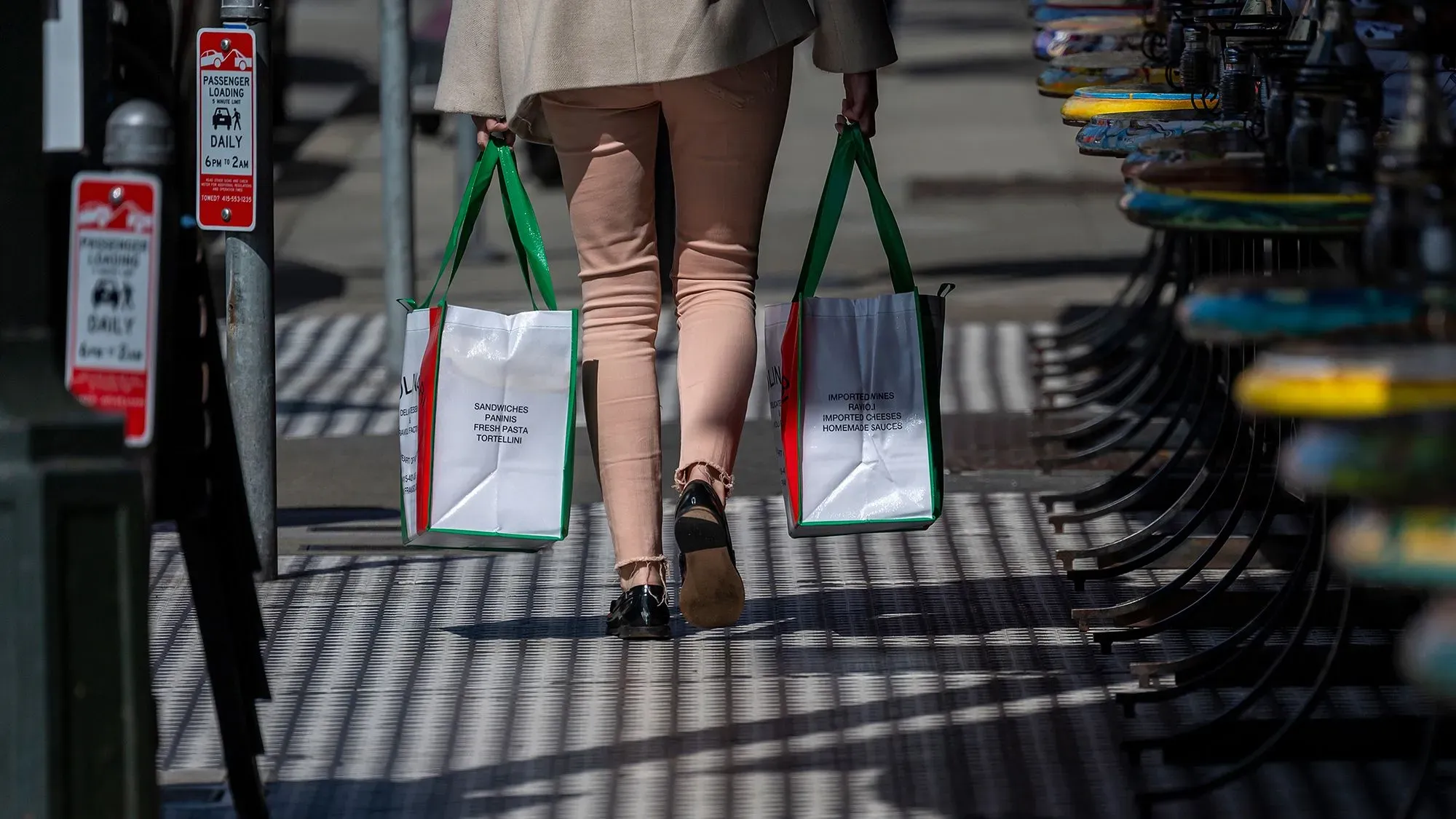 امرأة تحمل أكياس تسوق بينما تسير في الشارع، مما يعكس زيادة الإنفاق الاستهلاكي في ظل التغيرات الاقتصادية والسياسات التجارية.